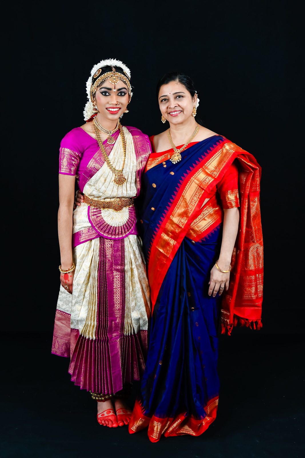 Arangetram dancer standing with a woman in a red and blue saree