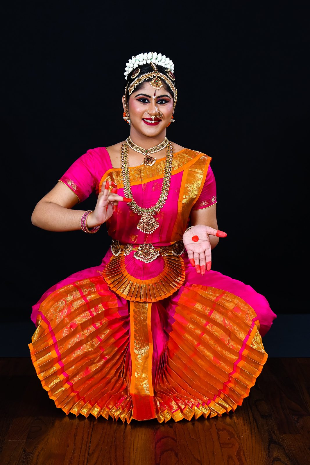 Arangetram dancer in pink and orange, seated pose