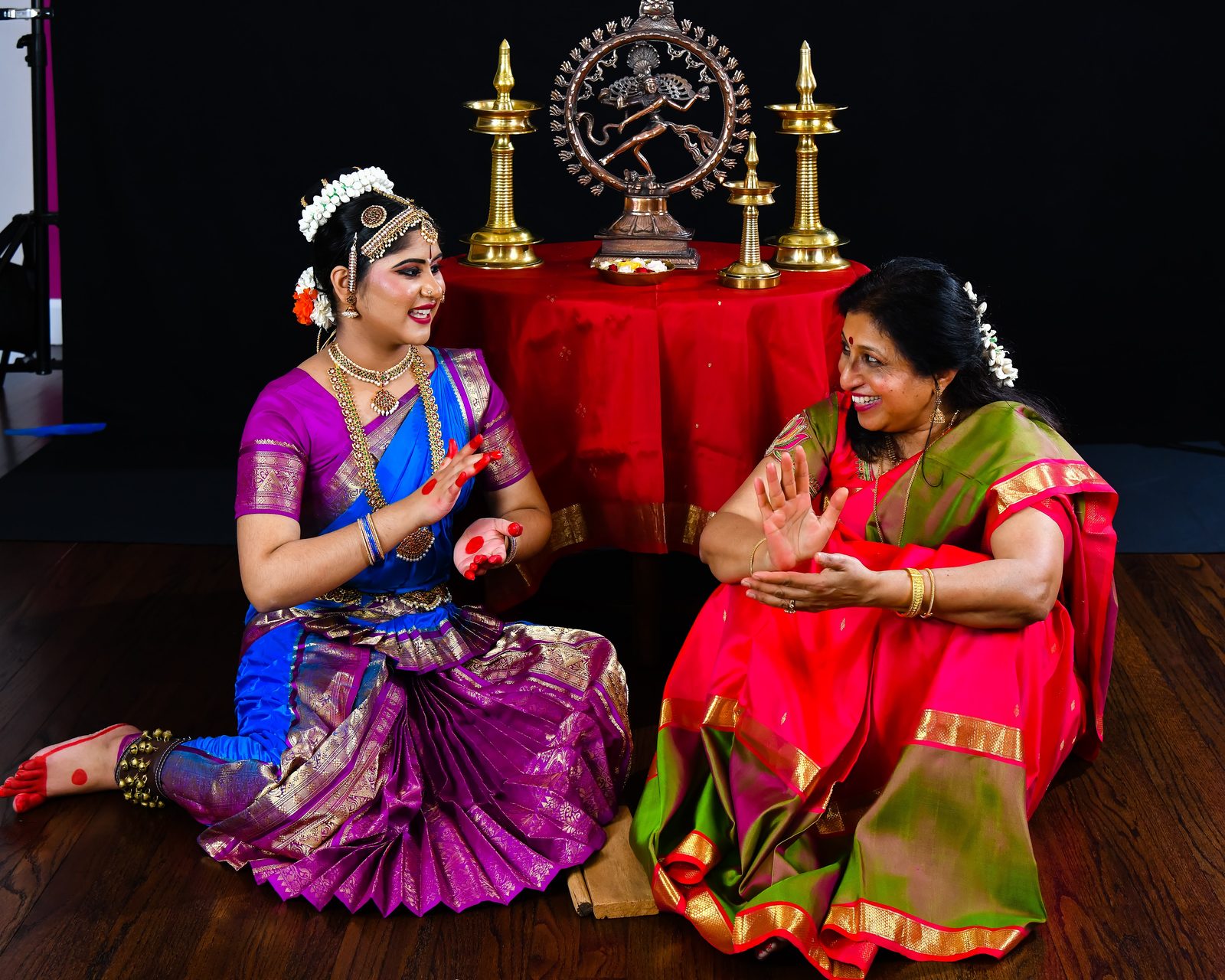 Arangetram dancer with her teacher beside a statue and brass lamps