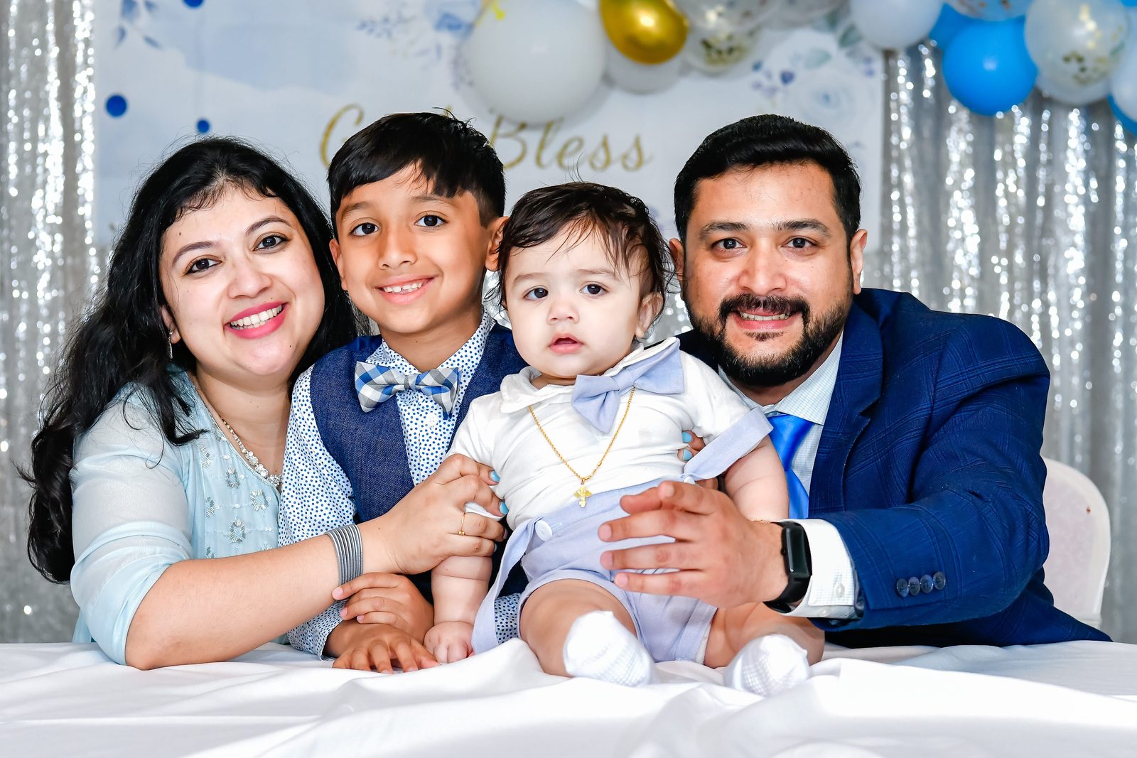 Family with their baby in front of a God Bless balloon backdrop