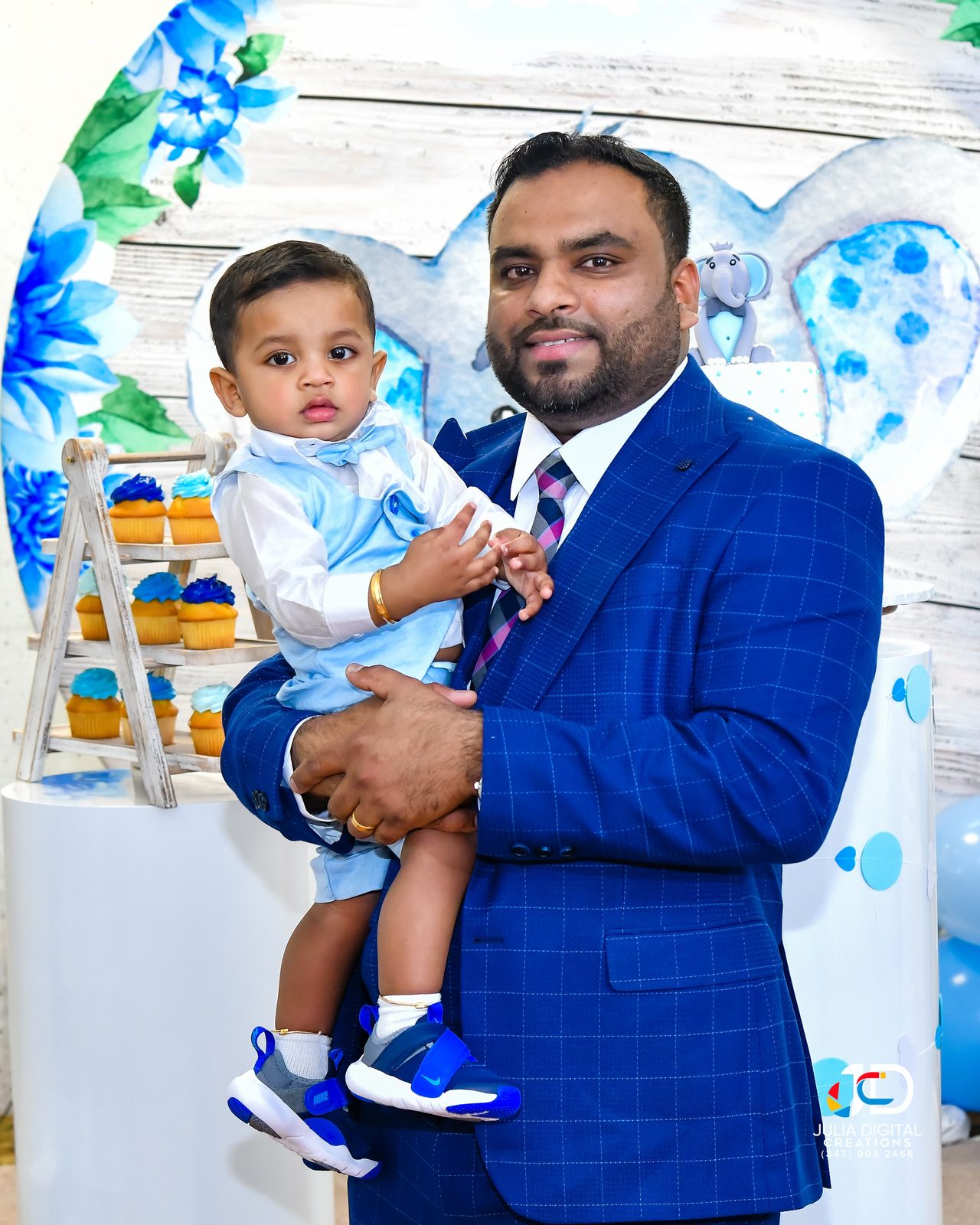 Father holding his toddler beside a birthday dessert table