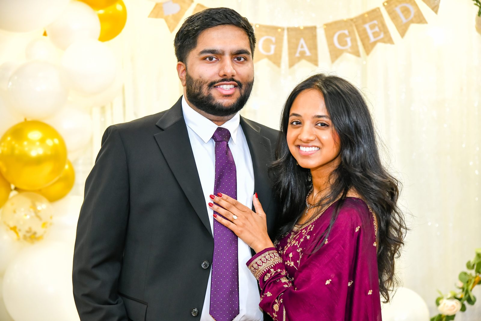 Engaged couple in front of a gold and white balloon backdrop
