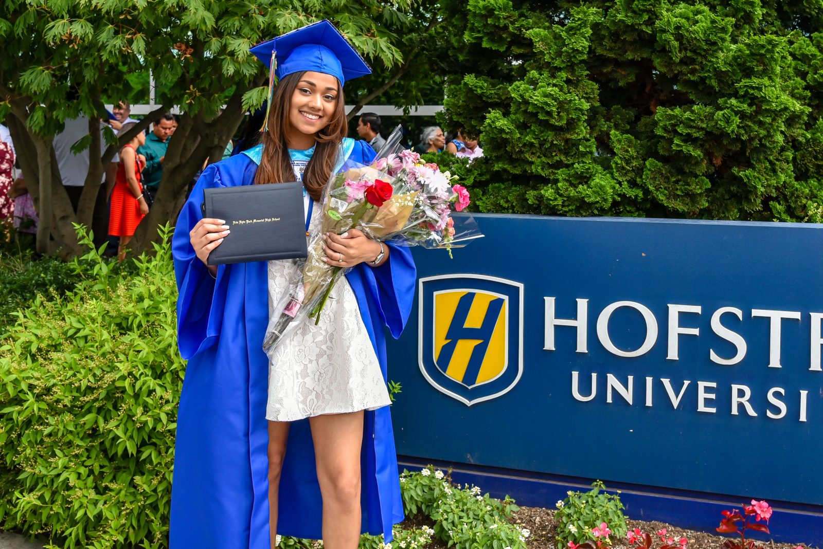 Graduate with her diploma and flowers at the Hofstra University sign