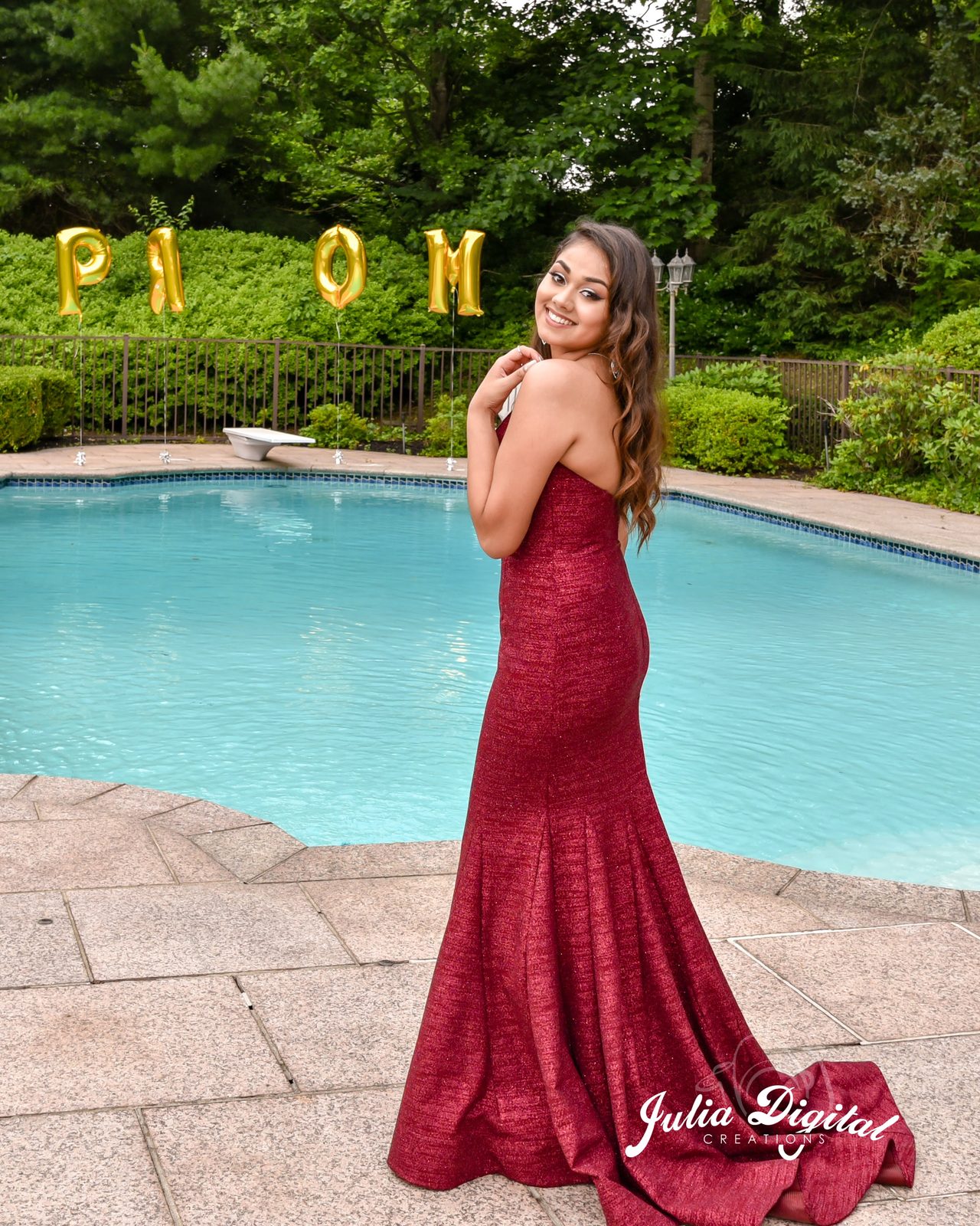 Prom portrait in a red gown by a pool with PROM balloons